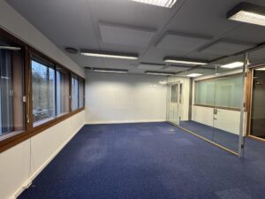 Modern empty office space on De Ruijterkade with blue carpet, glass walls, and large windows.